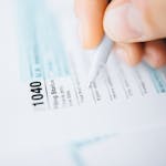 Herramientas PDF para trámites ¿Necesitas rellenar, firmar o convertir este documento en PDF? Usa nuestras herramientas gratuitas para preparar tu trámite.-up of a hand using a pen to fill out a tax form 1040, focusing on details.