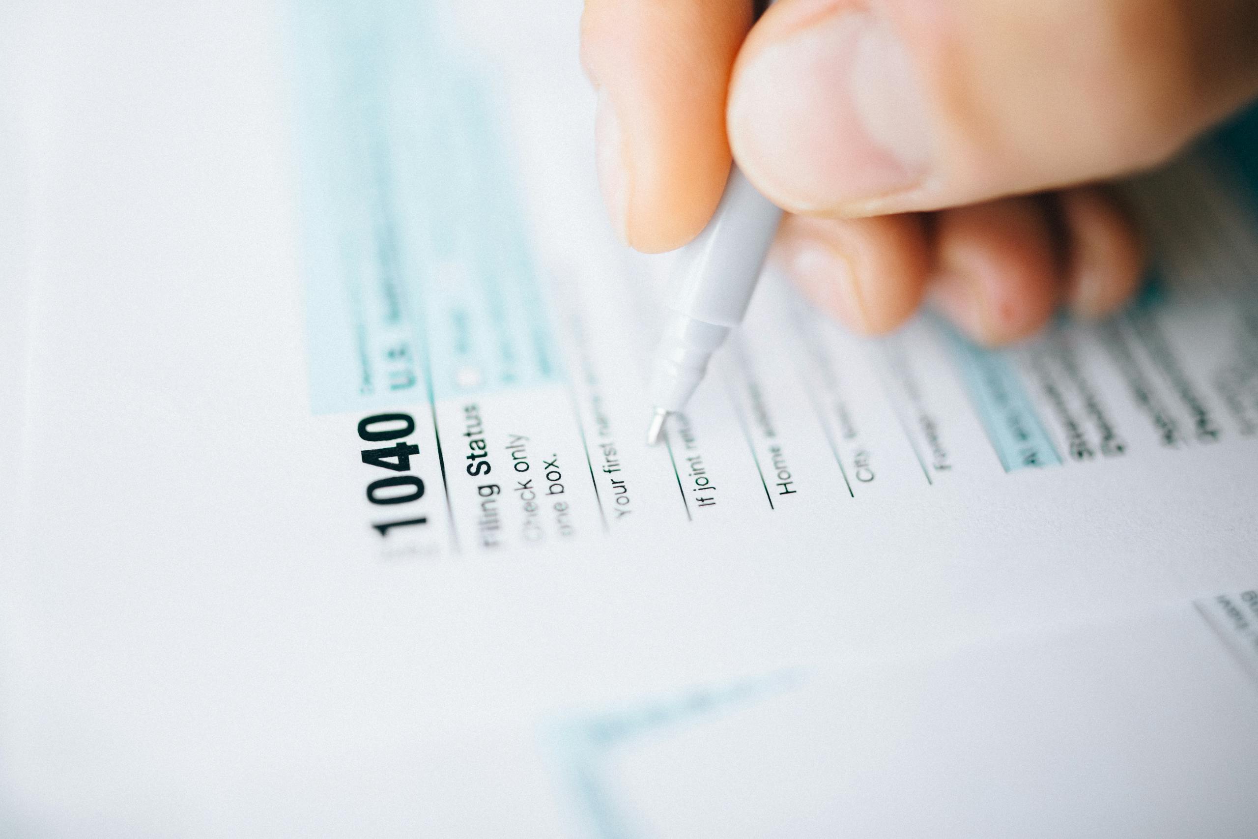 Herramientas PDF para trámites ¿Necesitas rellenar, firmar o convertir este documento en PDF? Usa nuestras herramientas gratuitas para preparar tu trámite.-up of a hand using a pen to fill out a tax form 1040, focusing on details.